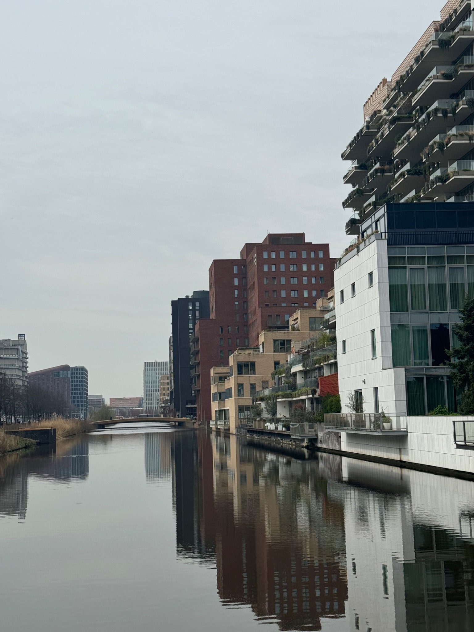 Nowoczesna architektura miejska: budynki mieszkalne z balkonami odbijają się w spokojnej wodzie kanału w pochmurny dzień.