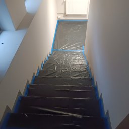 Mateusz Wiechowski - Schody zabezpieczone folią i taśmą malarską przed malowaniem ścian w jasnym wnętrzu, widok z góry.