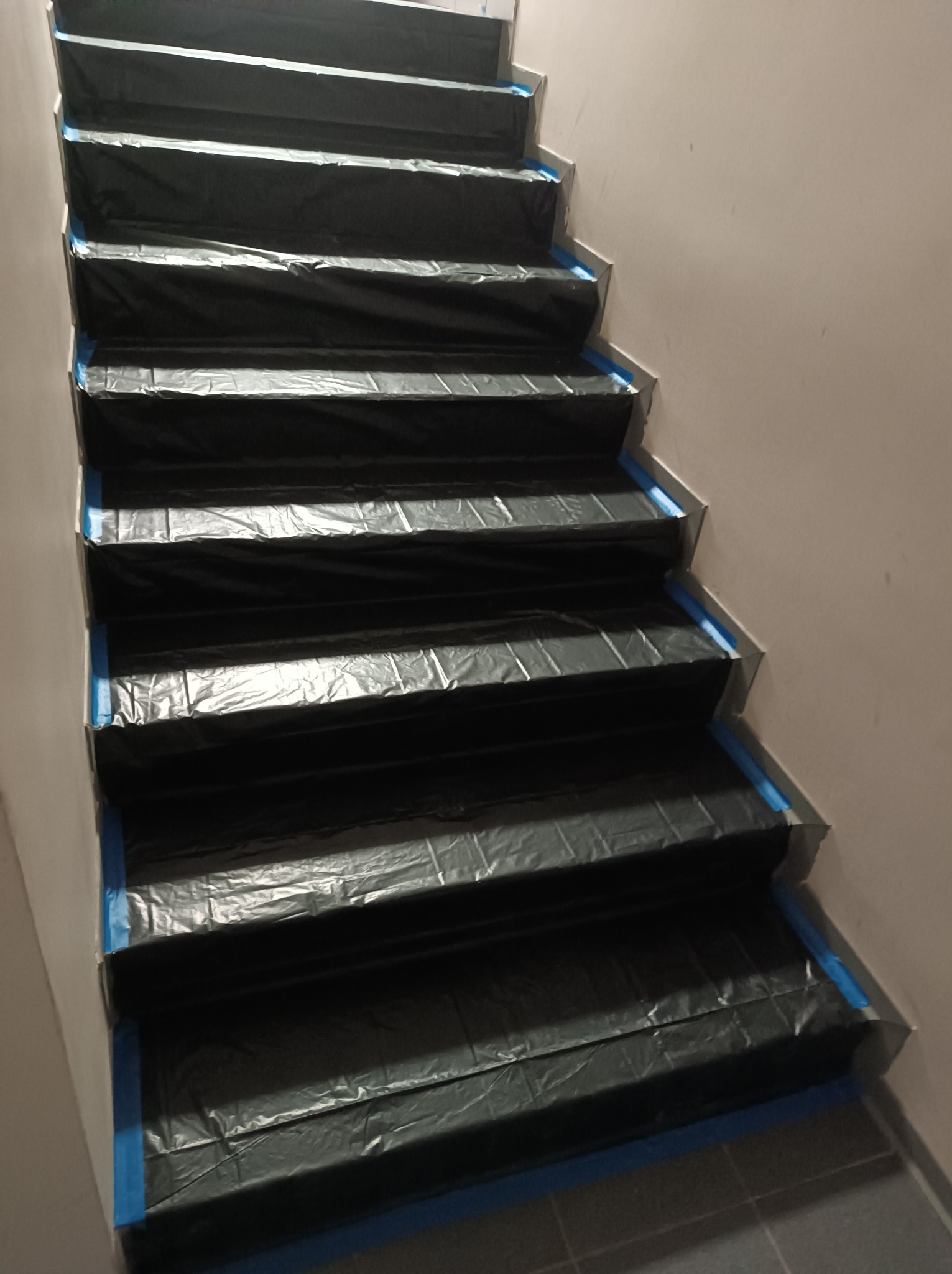 Schody zabezpieczone folią malarską i taśmą przed rozpoczęciem prac remontowych, widok z góry.