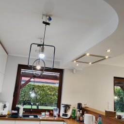 Budomex - Nowoczesna kuchnia z oknem na ogród, wisząca lampa z geometrycznym kloszem i podwieszany sufit z oświetleniem punktowym.