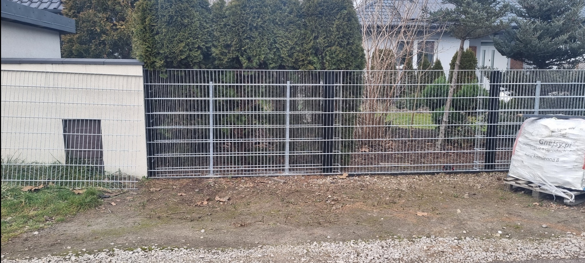 Nowoczesne ogrodzenie panelowe z podmurówką w Warszawie. Metalowa siatka, wysokie słupki, estetyczne wykończenie. Widok z zewnątrz posesji.