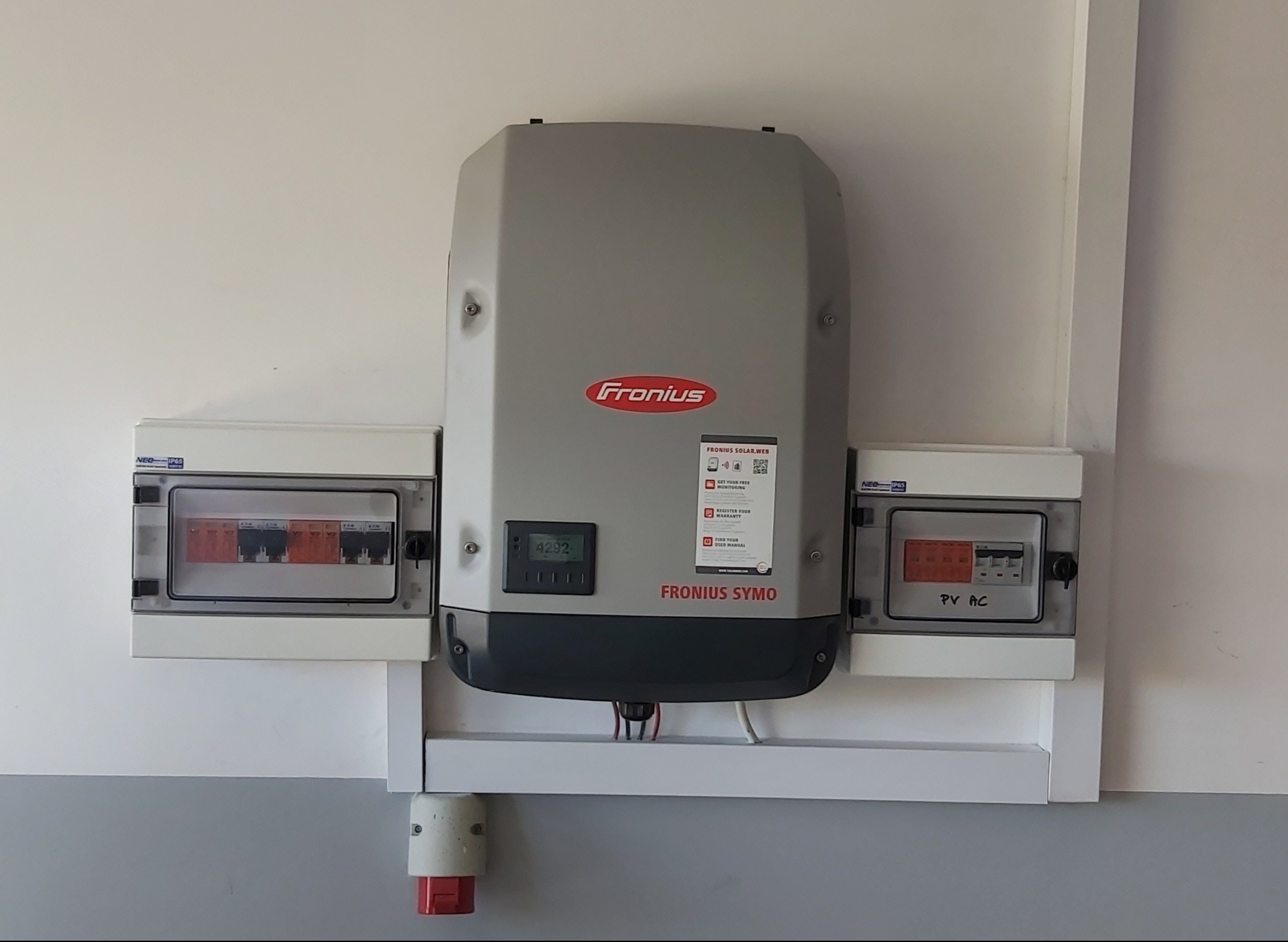 Szary falownik Fronius Symo zamontowany na ścianie w Sztumie, z widocznymi skrzynkami zabezpieczeń po bokach i wyświetlaczem pokazującym odczyt 4292.