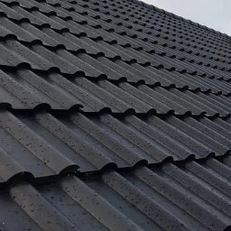 BIZNIER - BISHER ALSHAFEI - Czarny dach pokryty metalową blachodachówką z widocznymi kroplami deszczu, ujęcie z dołu pod kątem.