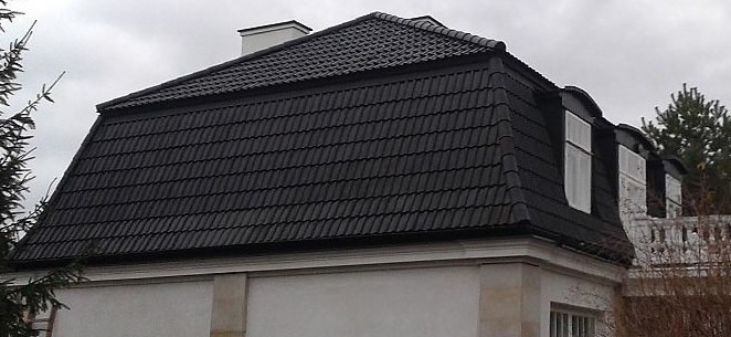 Czarny dach z lukarnami na jasnym budynku z kominem, widok z dołu.