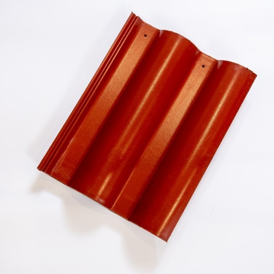 Pojedyncza, czerwona dachówka ceramiczna z widocznymi przetłoczeniami i dwoma otworami montażowymi, leżąca na białym tle.