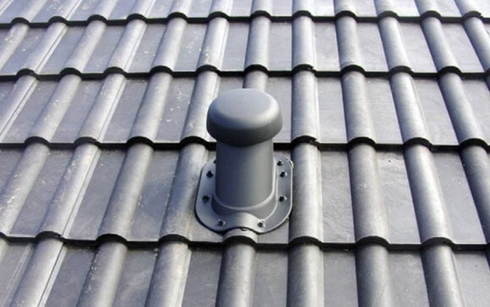 Szare, ceramiczne pokrycie dachowe z zamontowanym, ciemnym kominkiem wentylacyjnym, widoczne śruby mocujące.