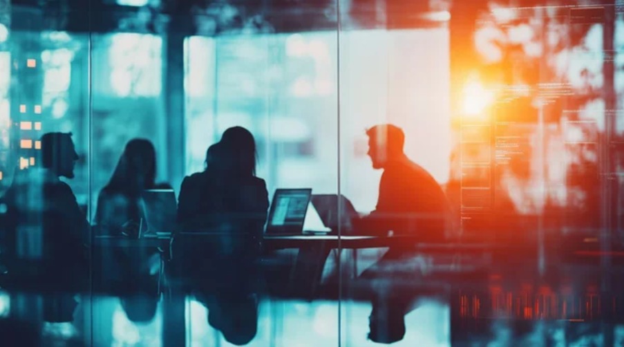 Silhouettes of people working on laptops in a modern office setting, with a bright, abstract overlay of data visualizations and code, creating a futuristic and dynamic atmosphere.