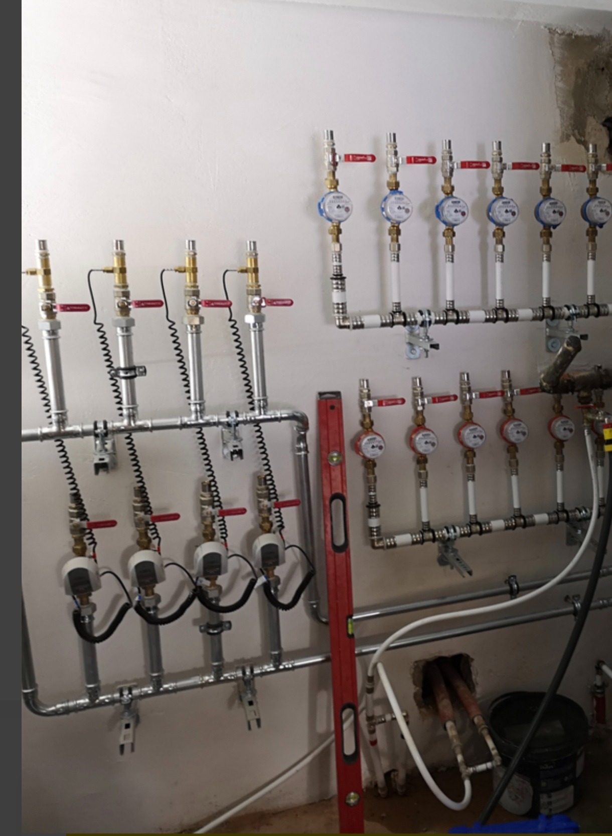 Rozdzielacz z licznikami ciepła zamontowany na ścianie, widoczny poziomica, instalacja w surowym stanie.