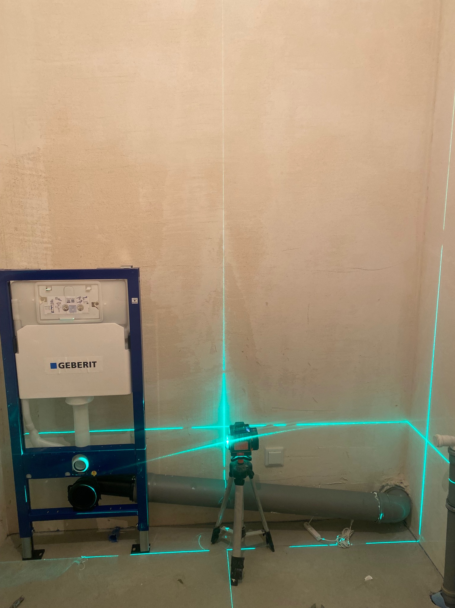 Stelaż podtynkowy Geberit zamontowany w surowej łazience, poziomowany laserowo przed obudowaniem, widoczne szare rury kanalizacyjne.