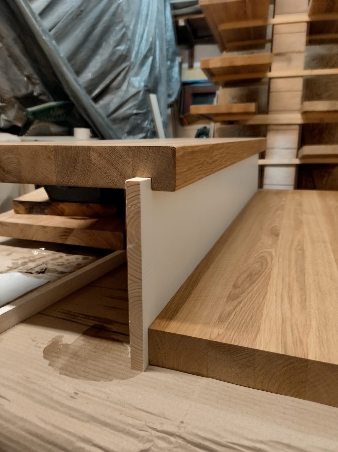 Detal drewnianych schodów z białymi podstopnicami w trakcie montażu, widoczne elementy konstrukcyjne i zaplecze warsztatowe.