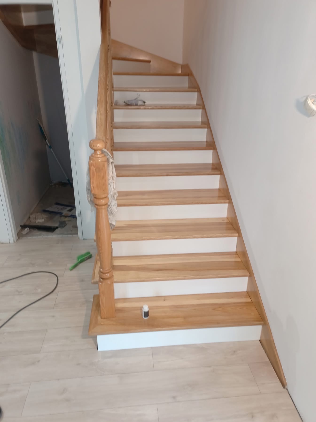 Jasne, drewniane schody z białymi podstopnicami w trakcie montażu, widoczne narzędzia i materiały budowlane w tle.