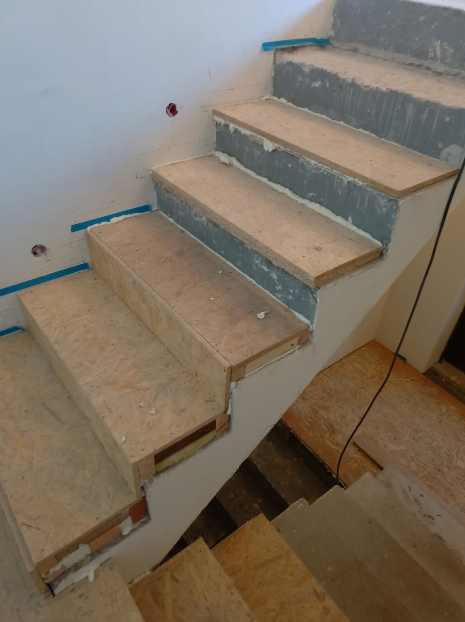 Surowe schody w trakcie budowy z płyt OSB przytwierdzonych do betonowej konstrukcji, widoczne ślady pianki montażowej i taśmy malarskiej.