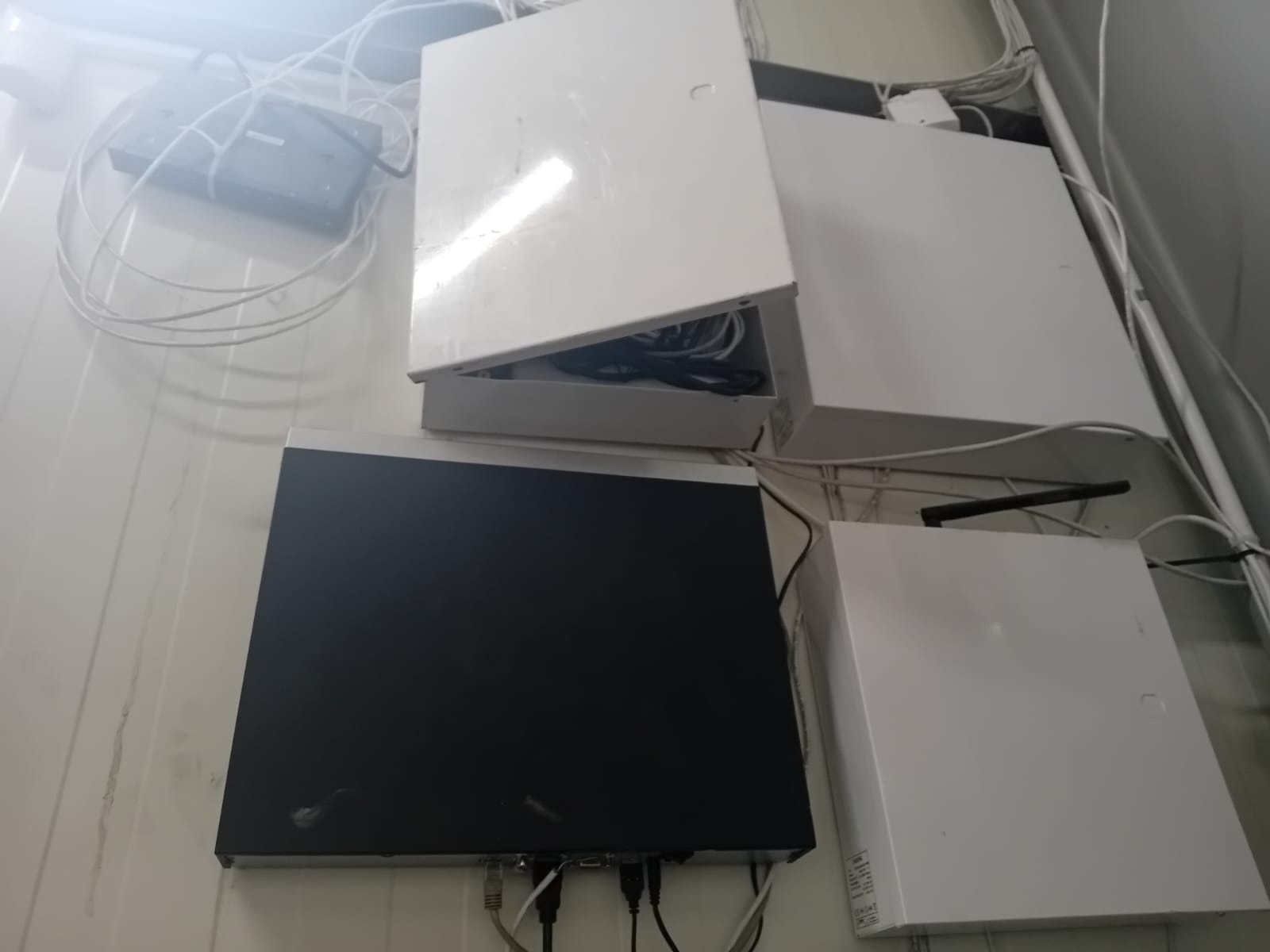 Zamontowane na ścianie skrzynki i urządzenia elektroniczne, prawdopodobnie związane z monitoringiem lub alarmem, widoczne kable i otwarte wieko jednej ze skrzynek.