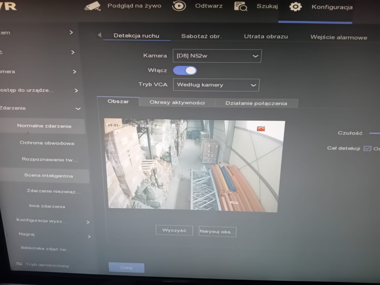 Ekran monitora z ustawieniami detekcji ruchu kamery przemysłowej, widok z kamery na magazyn z regałami i towarem.