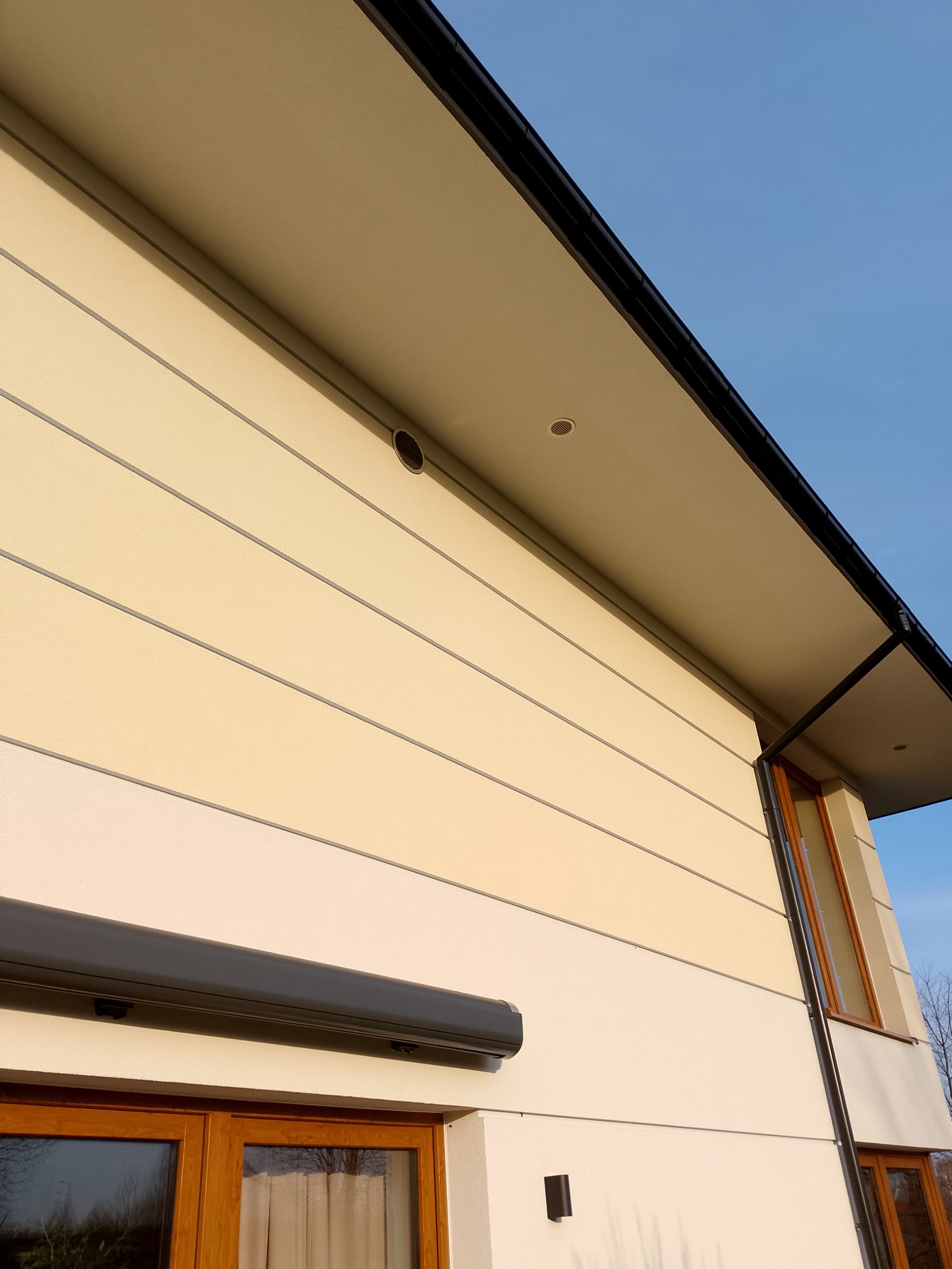 Elewacja budynku z widocznym otworem wentylacyjnym pod okapem i roletą zewnętrzną, okna z drewnianą stolarką.