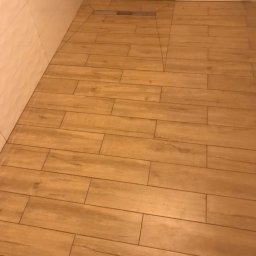 Norbert - Ułożona podłoga z płytek imitujących drewno w łazience z odpływem liniowym.