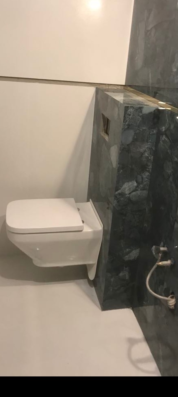 Nowoczesna, podwieszana toaleta z białą deską, zamontowana na tle ściany wykończonej płytami imitującymi ciemny marmur. Widoczne elementy instalacji wodnej.