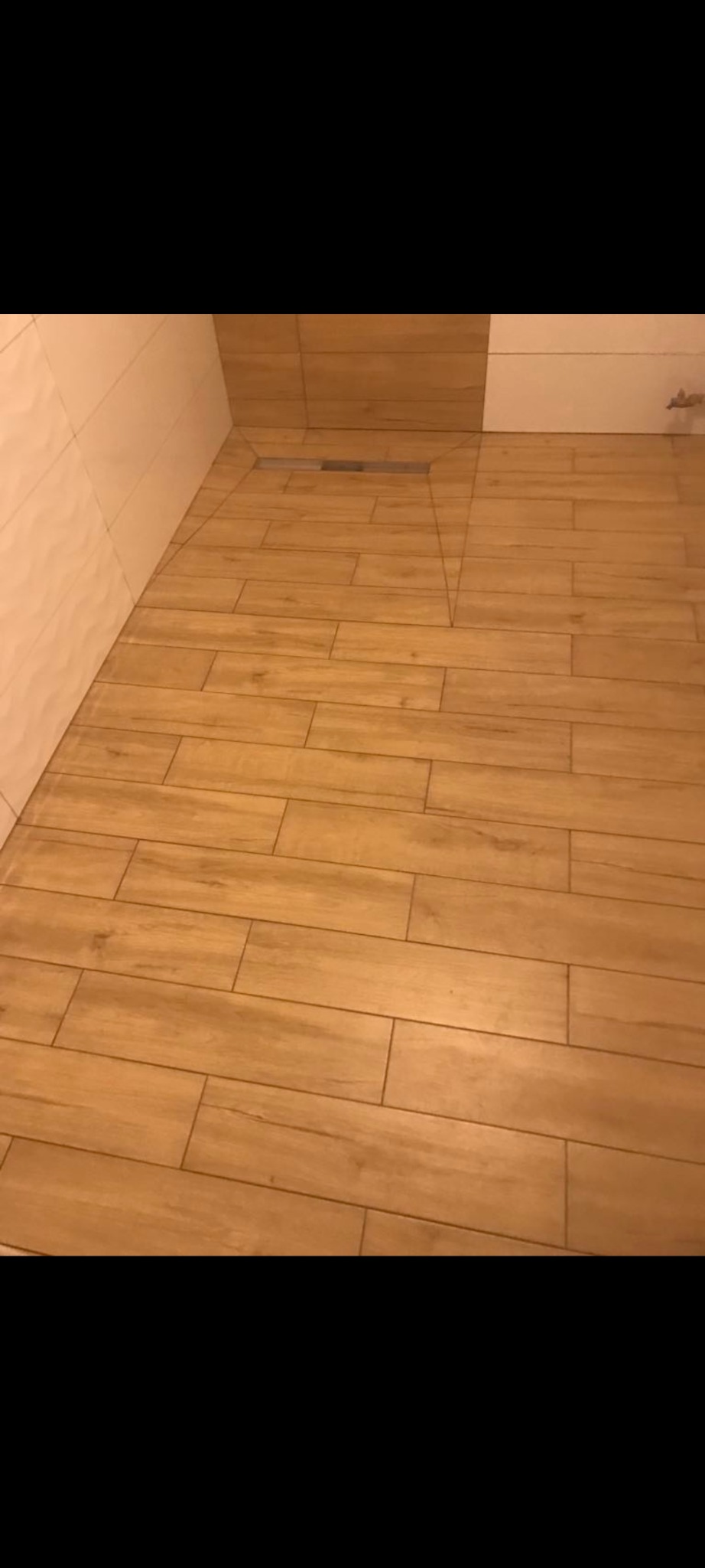 Ułożona podłoga z płytek imitujących drewno w łazience z odpływem liniowym.