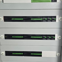 CEIRON SPÓŁKA Z OGRANICZONĄ ODPOWIEDZIALNOŚCIĄ - Rozdzielnia elektryczna z modułami Loxone, widoczne bezpieczniki i moduły sterujące systemem inteligentnego domu, szara obudowa z białymi elementami mocującymi.