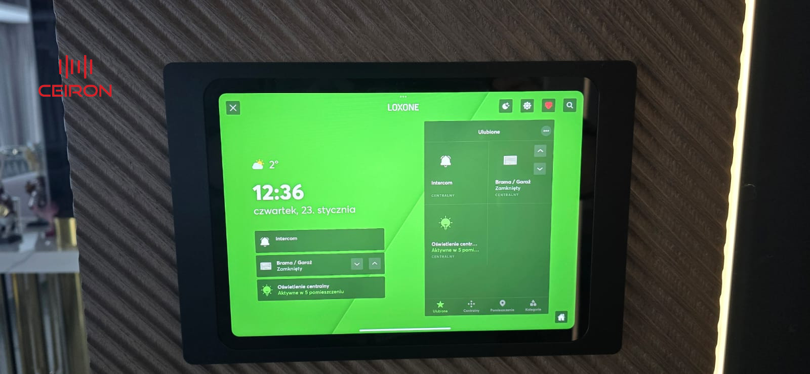Panel sterowania Loxone zamontowany na ścianie z widocznym interfejsem użytkownika, prezentującym stan bramy, intercomu i oświetlenia centralnego.