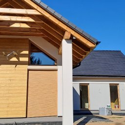 LIS-BUD BARTŁOMIEJ LISIECKI - Nowoczesny dom jednorodzinny z drewnianą elewacją, roletami zewnętrznymi i oknem o nietypowym kształcie, w trakcie wykańczania, widoczne materiały budowlane.