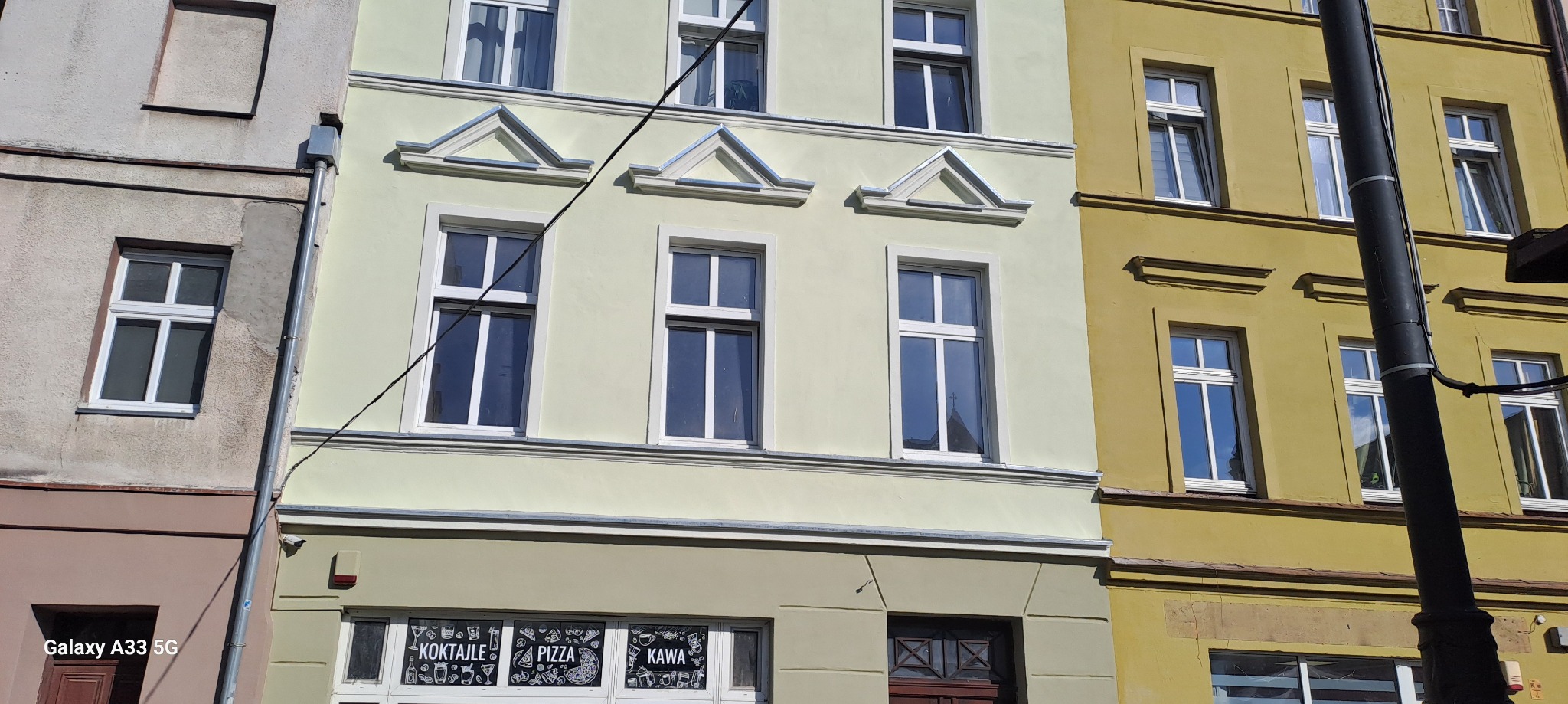 Fasada kamienicy z oknami po renowacji, widoczne detale architektoniczne i odświeżona kolorystyka elewacji sąsiadujących budynków