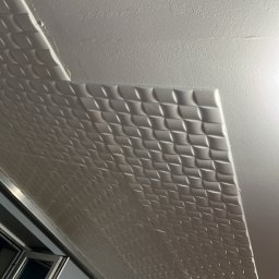 SpecINSTAL Adrian Strugała - Fragment sufitu z zamontowanymi białymi panelami 3D o wzorze rombów, widoczne okno w tle, oświetlenie górne.