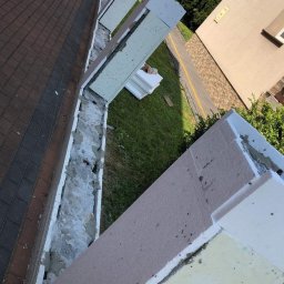 SpecINSTAL Adrian Strugała - Fragment elewacji budynku w trakcie ocieplania, widoczne płyty styropianowe, warstwa kleju i siatki, przygotowane do dalszych prac wykończeniowych, z widocznym fragmentem chodnika i trawnika w tle.