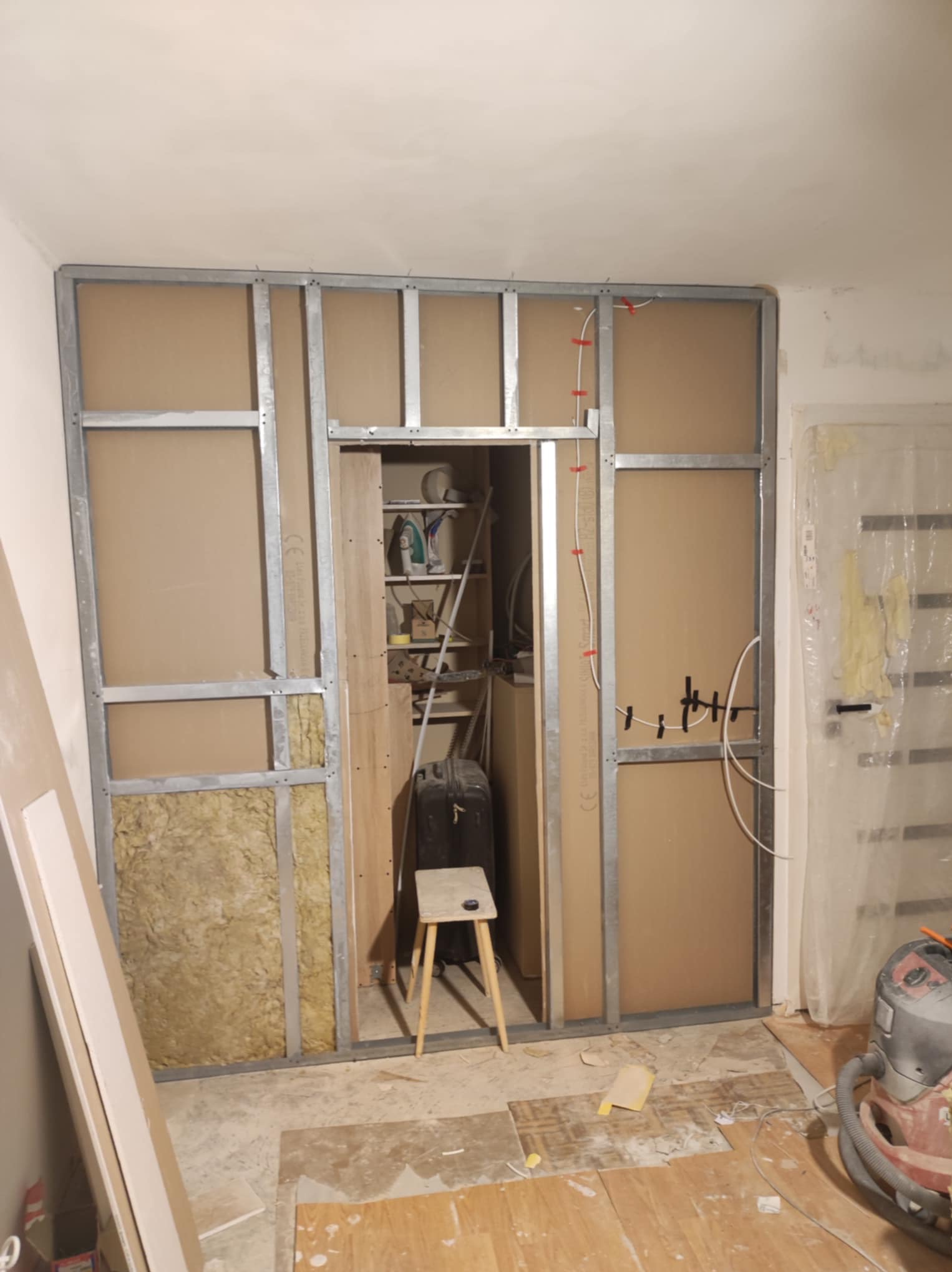 Wnętrze w trakcie tworzenia ścianki działowej z metalowym szkieletem, wypełnionym wełną mineralną, z widocznym otworem drzwiowym i instalacją elektryczną, na podłodze resztki materiałów budowlanych...