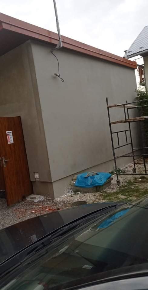 Świeżo otynkowana elewacja budynku z drewnianymi drzwiami i metalowym rusztowaniem, widok zza szyby samochodu.