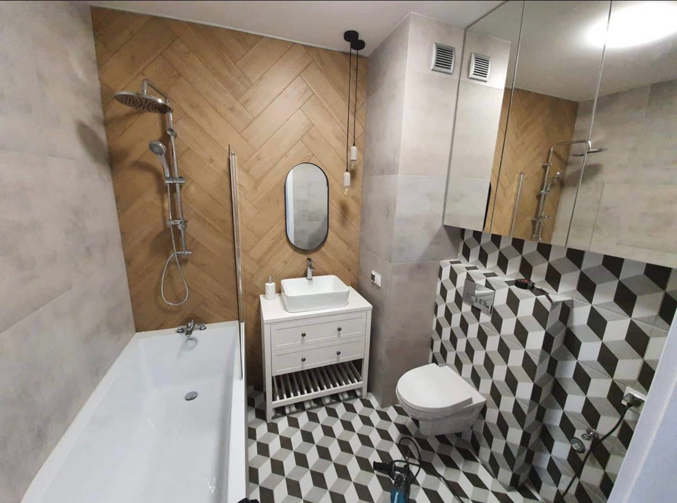 Wykończona łazienka z drewnopodobną ścianą, białą armaturą i geometrycznymi płytkami. Uwagę zwraca nietypowy wzór płytek podłogowych i ściennych.