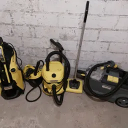 Żółto-czarne odkurzacze Karcher, w tym piorący, stoją pod ścianą z cegieł, gotowe do użycia w usłudze sprzątania.