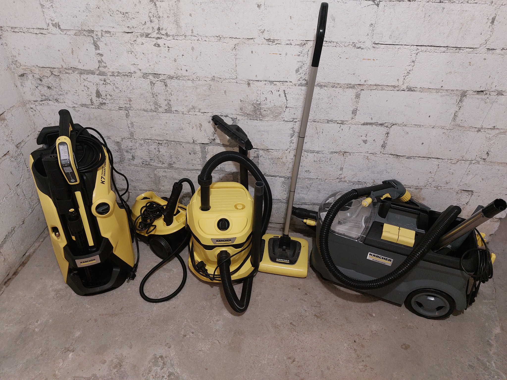 Żółto-czarne odkurzacze Karcher, w tym piorący, stoją pod ścianą z cegieł, gotowe do użycia w usłudze sprzątania.