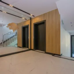 Wnętrze apartamentowca Uzdrowiskowe HYGGE z dwoma windami, marmurową posadzką i lustrem odbijającym schody.