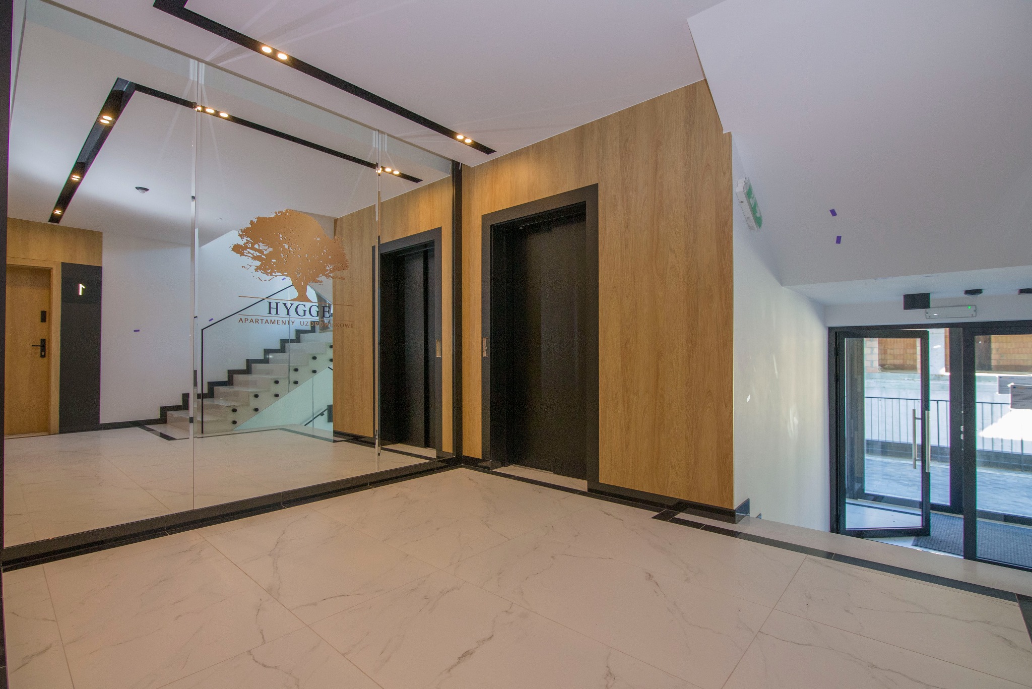 Wnętrze apartamentowca Uzdrowiskowe HYGGE z dwoma windami, marmurową posadzką i lustrem odbijającym schody.