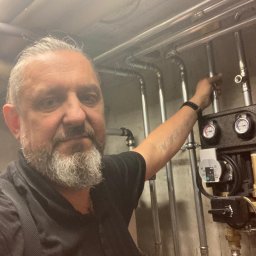 ECO ANGELS SOLUTIONS SPÓŁKA Z OGRANICZONĄ ODPOWIEDZIALNOŚCIĄ - Instalator prezentuje zamontowany system rur i urządzeń, prawdopodobnie związanych z ogrzewaniem lub instalacją wodną. Widoczny manometr i pompa obiegowa.