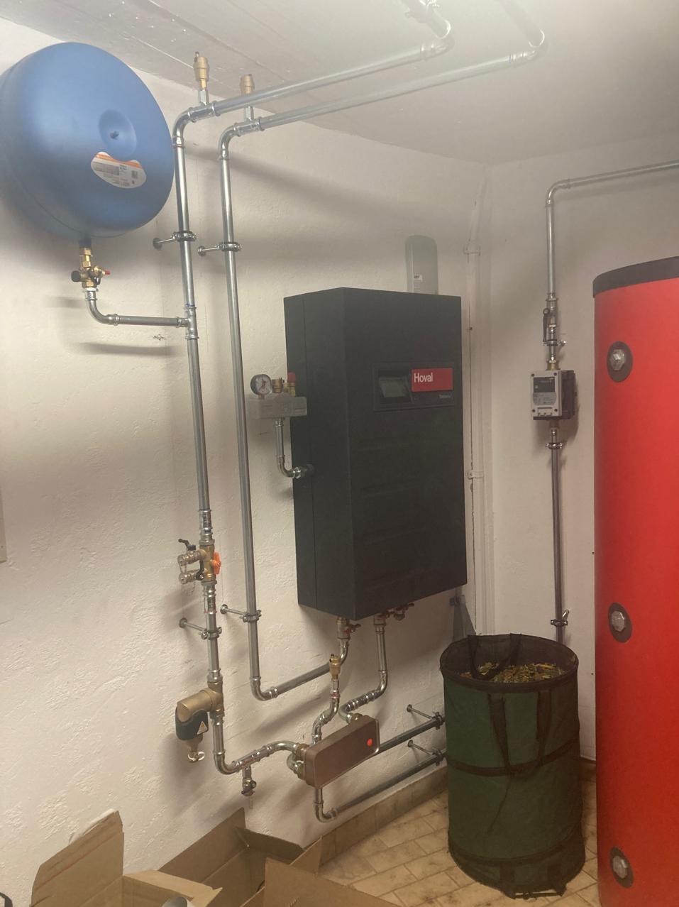 Złożona instalacja grzewcza z piecem Hoval i zbiornikiem w Morzyczynie. Widoczne rury, zawory i osprzęt. Całość zamontowana na białej ścianie w pomieszczeniu.