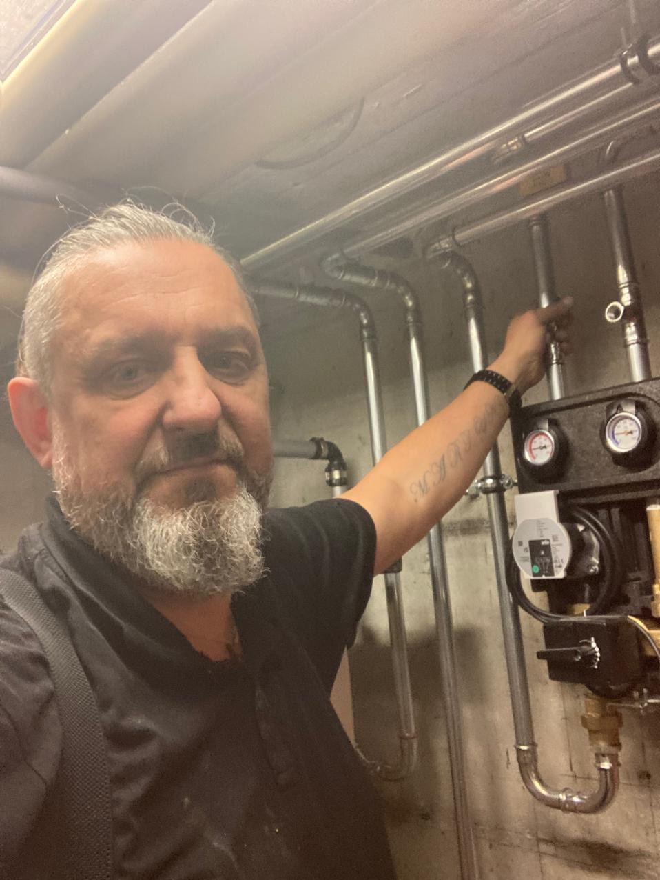 Instalator prezentuje zamontowany system rur i urządzeń, prawdopodobnie związanych z ogrzewaniem lub instalacją wodną. Widoczny manometr i pompa obiegowa.