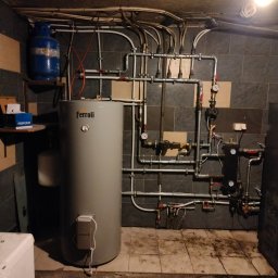 BE-ENERGY - Instalacja CO z zbiornikiem Ferroli, rurami i osprzętem w kotłowni w Przejazdowie. Widoczny manometr i butla gazowa na półce.