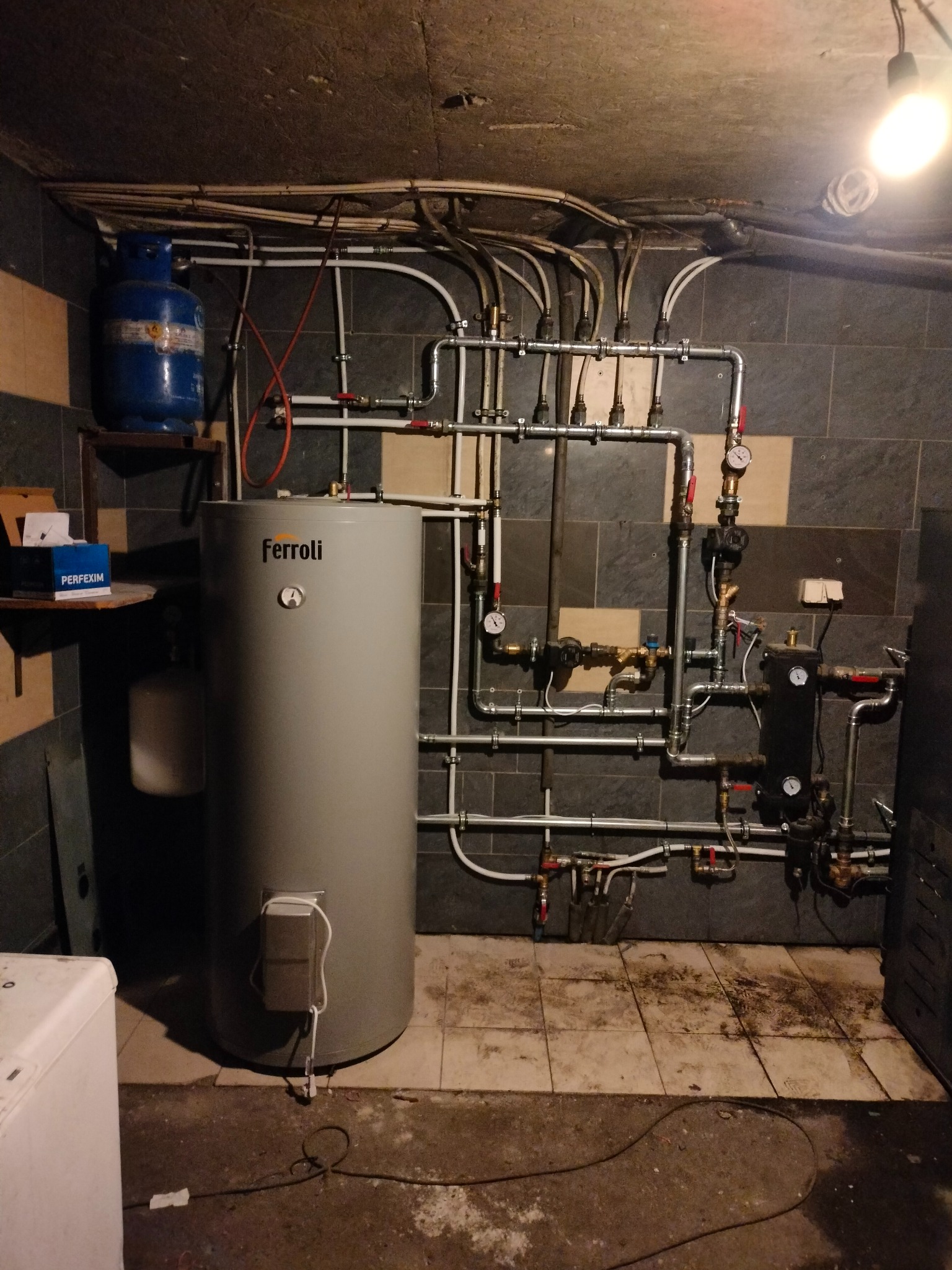 Instalacja CO z zbiornikiem Ferroli, rurami i osprzętem w kotłowni w Przejazdowie. Widoczny manometr i butla gazowa na półce.
