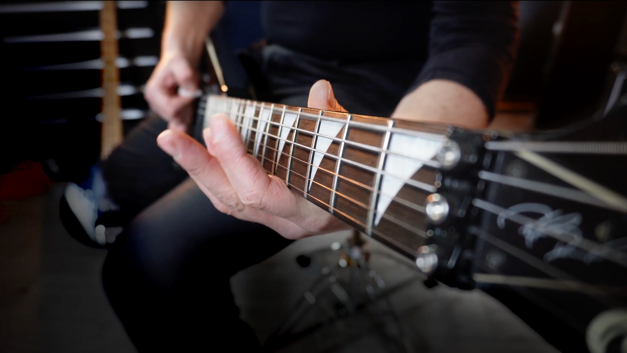 Bliski plan dłoni grającej na gitarze elektrycznej z białymi inkrustacjami na gryfie, uchwycony z perspektywy gracza.