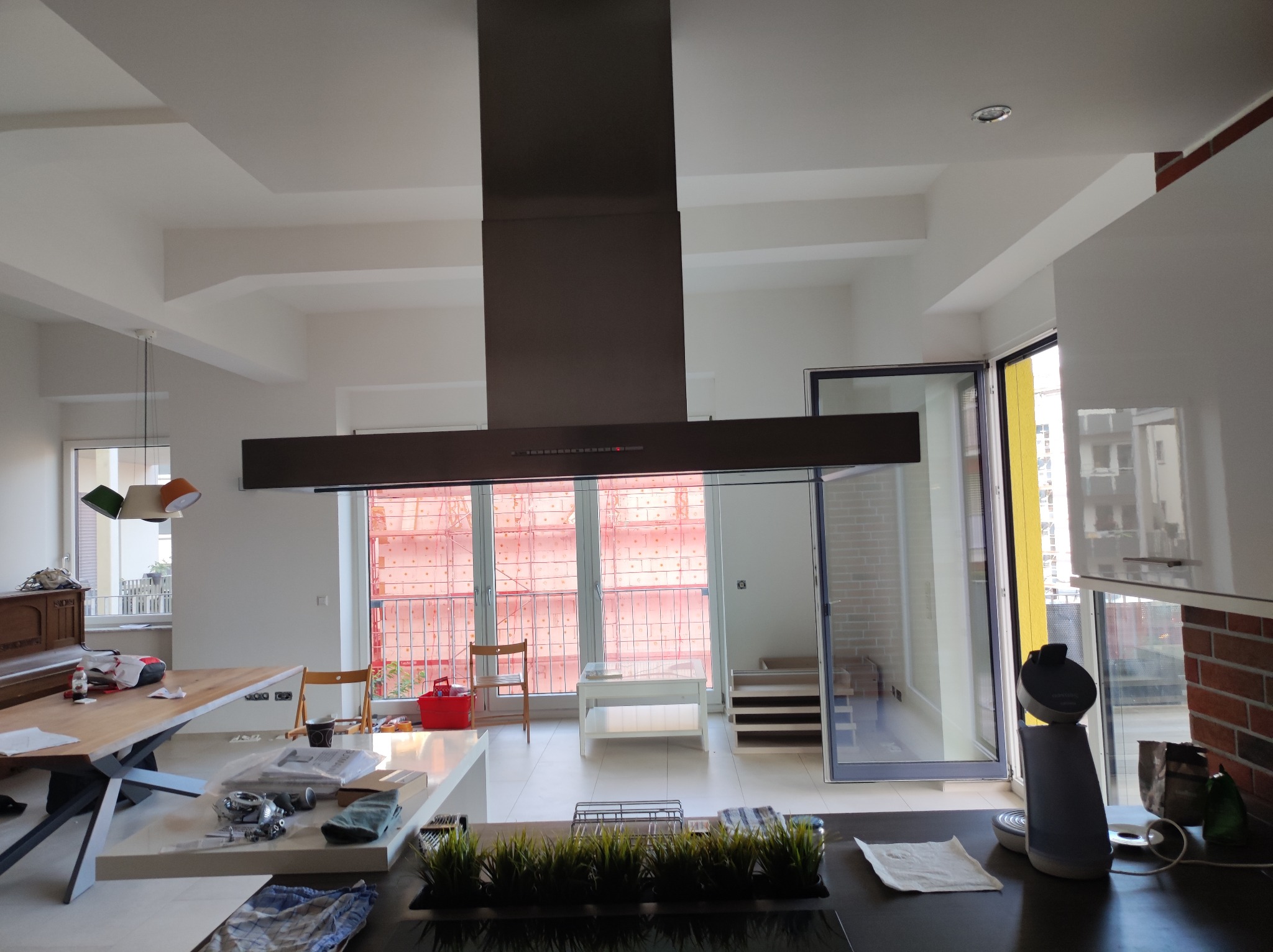 Nowoczesna kuchnia w trakcie remontu: widoczny duży okap nad wyspą kuchenną, na blacie akcesoria kuchenne, w tle rusztowania za oknem.