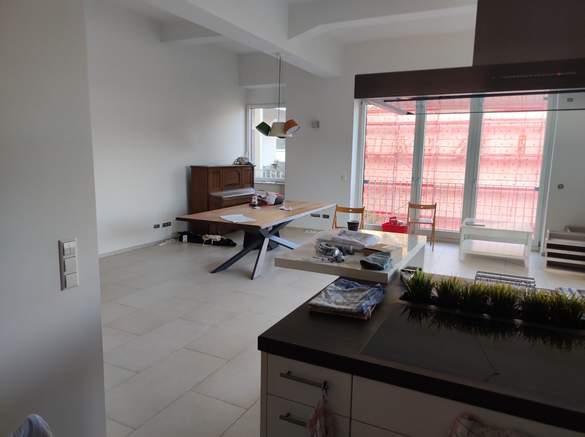 Wnętrze mieszkania w trakcie remontu: widoczne rusztowania za oknem, niepomalowane ściany, meble częściowo zakryte, przygotowane do malowania.