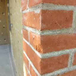 Fragment nowo wymurowanej ściany z czerwonej cegły, widoczna warstwa izolacji na sąsiedniej ścianie.