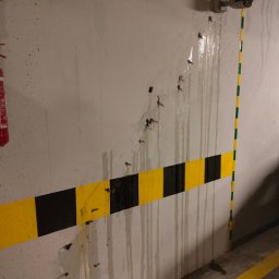 Prime-tech - Ściana w garażu z widocznymi śladami po wierceniu, zabezpieczona pasem ostrzegawczym, z zamontowaną kamerą przemysłową i instalacją elektryczną.
