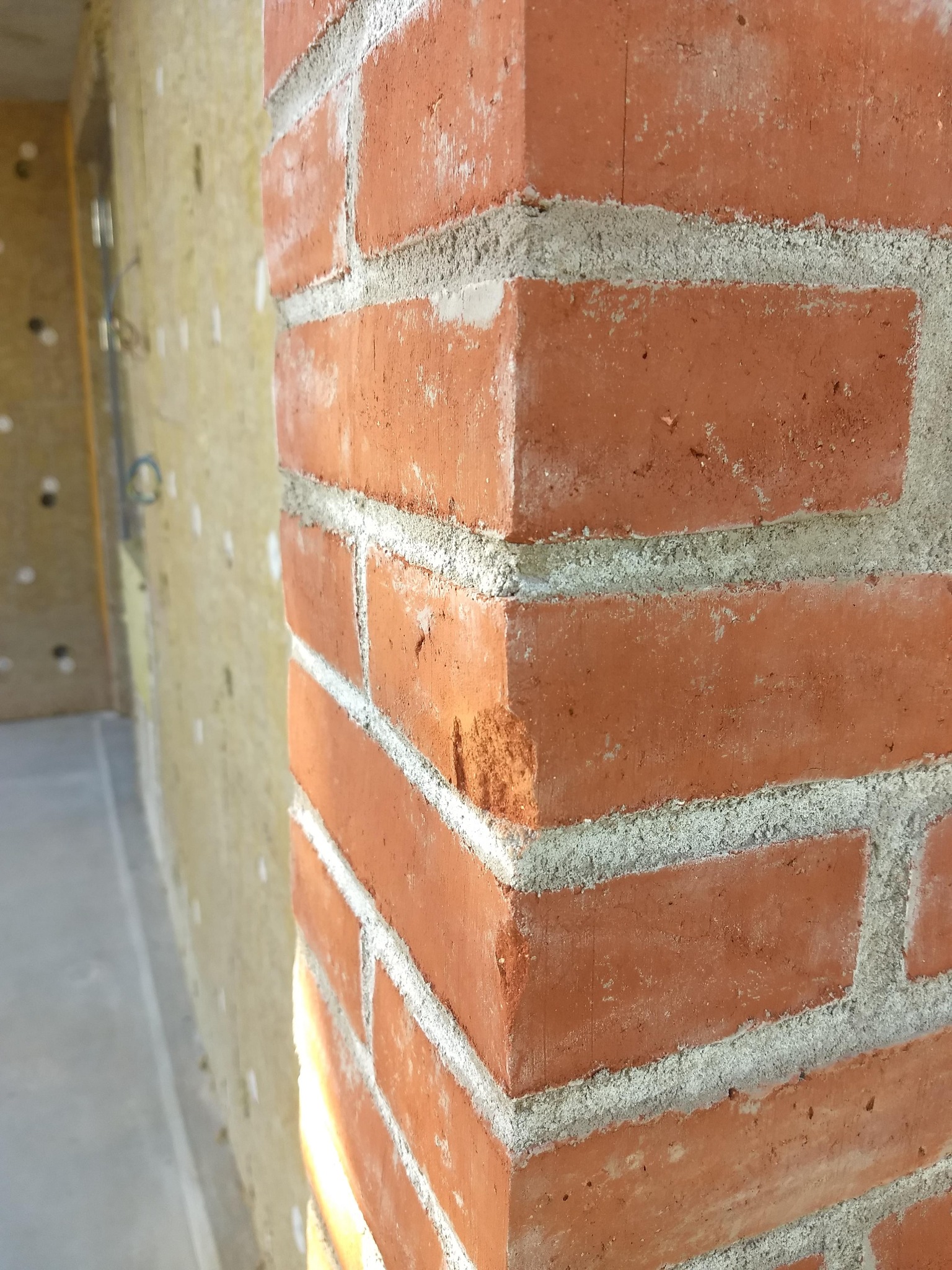 Fragment nowo wymurowanej ściany z czerwonej cegły, widoczna warstwa izolacji na sąsiedniej ścianie.