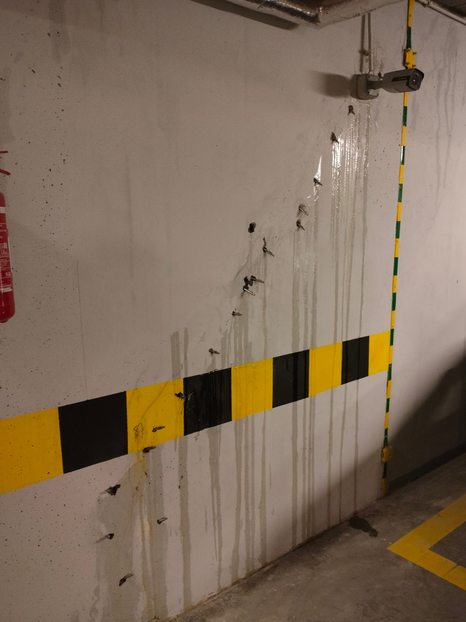 Ściana w garażu z widocznymi śladami po wierceniu, zabezpieczona pasem ostrzegawczym, z zamontowaną kamerą przemysłową i instalacją elektryczną.