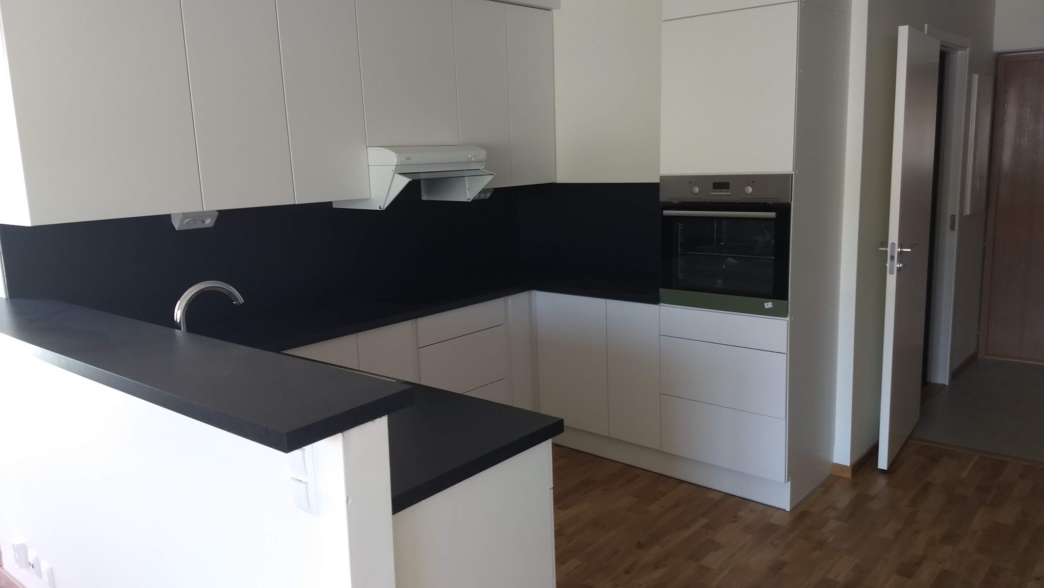 Nowoczesna kuchnia z białymi szafkami i czarnym blatem, widoczny zlewozmywak, okap i piekarnik, podłoga z paneli.