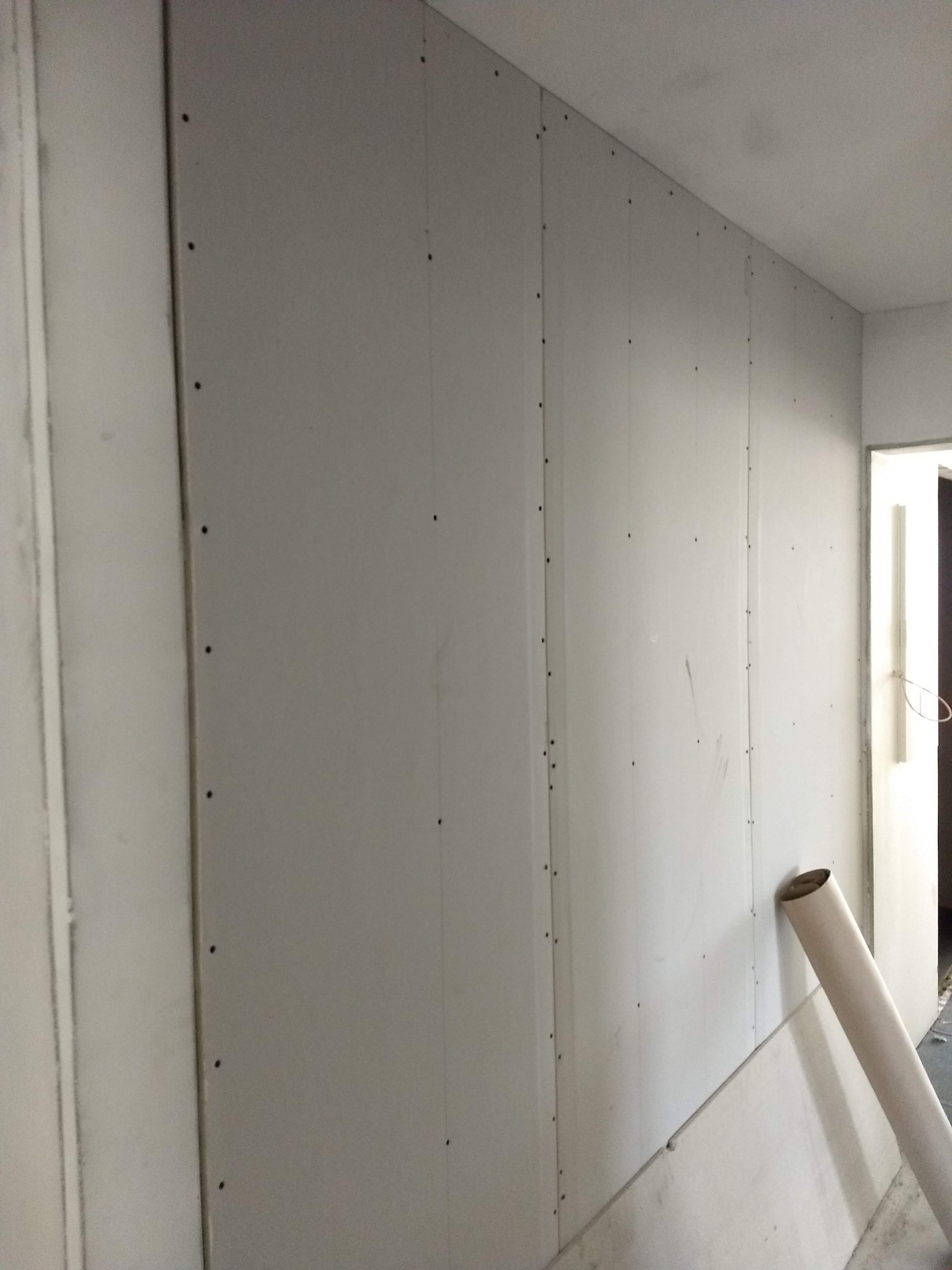 Ściana z zamontowanych płyt kartonowo-gipsowych, widoczne wkręty mocujące, na podłodze leży zwinięty rulon papieru.