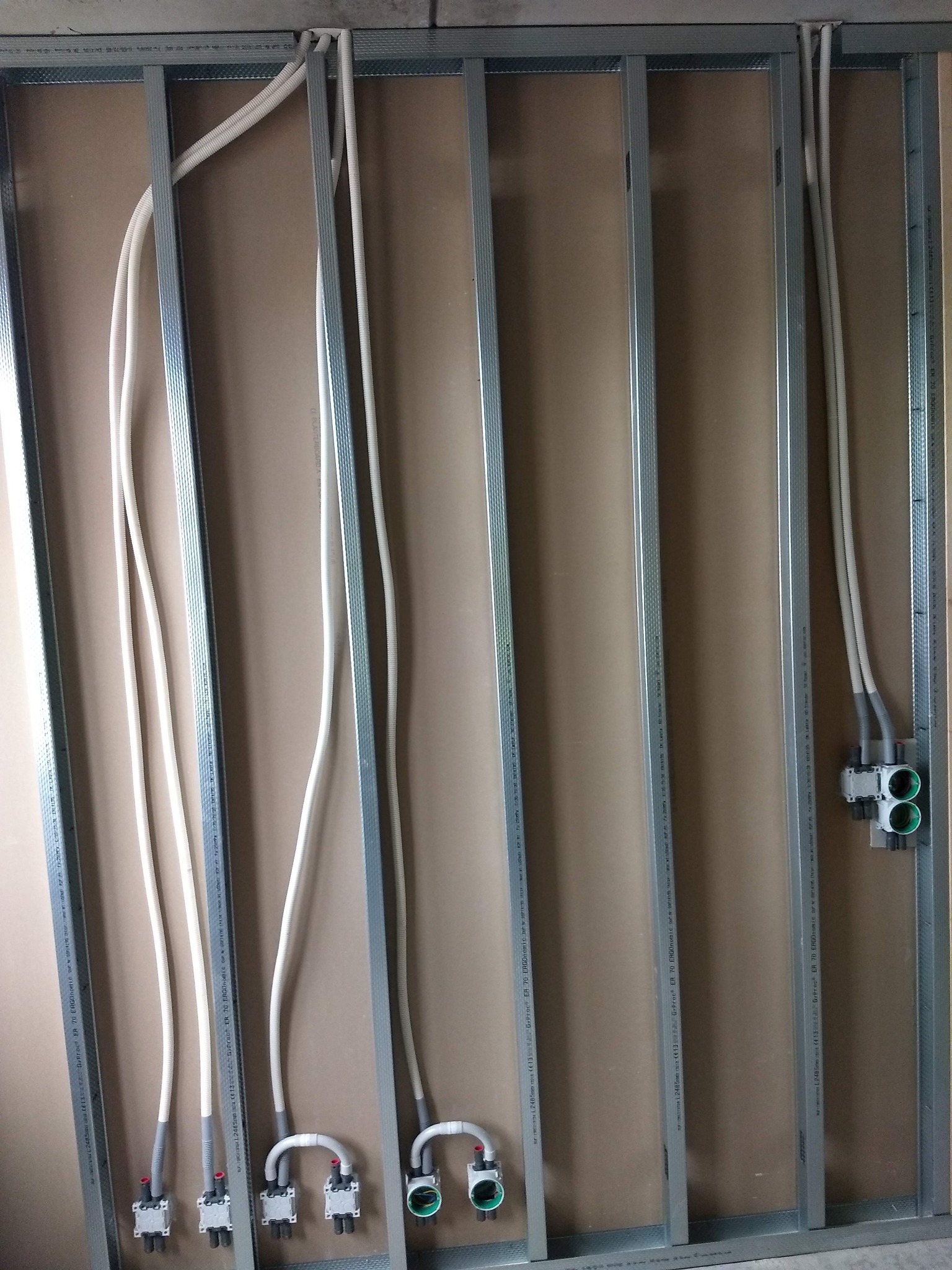 Konstrukcja ściany z profili metalowych, z zamontowanymi przewodami instalacji wodnej i elektrycznej, przed położeniem płyty kartonowo-gipsowej.